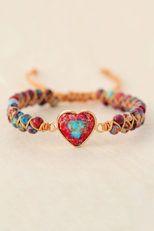 Multicolored beaded bracelet with a heart-shaped red and gold clasp on a beige background