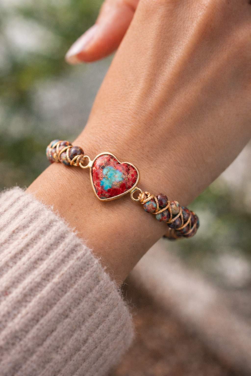 Bracelet with a heart-shaped red stone and gold accents on a wrist.
